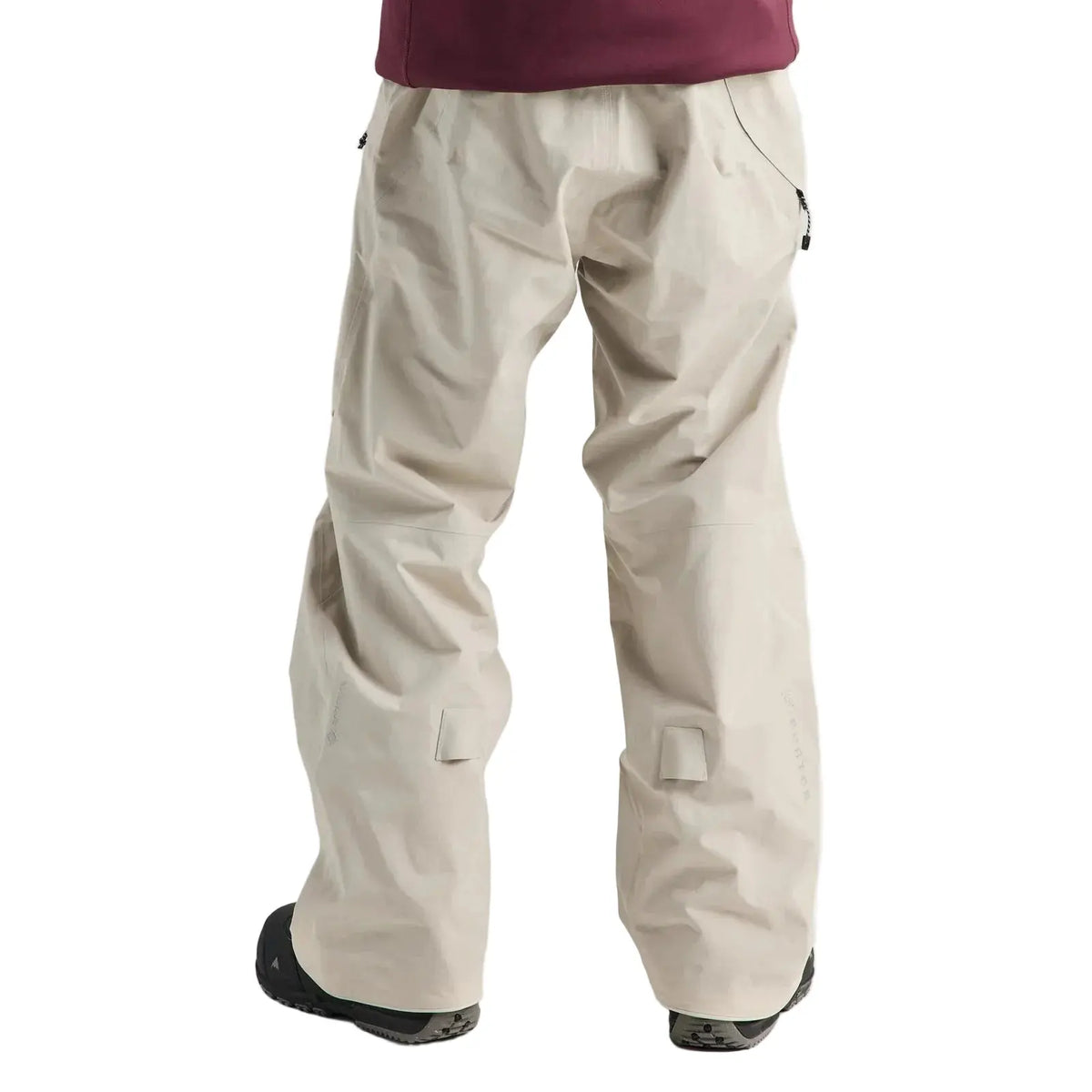 A person shown from the back wearing light beige technical snowboard pants, a dark burgundy top, and black boots against a plain light gray studio background.