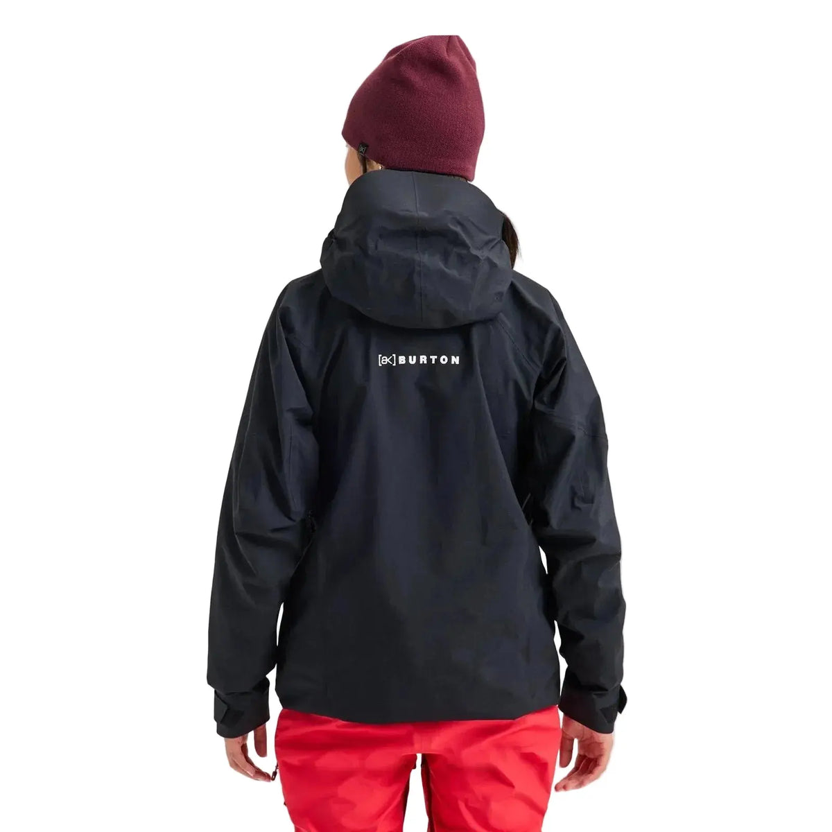 A person shown from the back wearing a black Burton hooded jacket, a burgundy beanie, and bright red pants against a light gray studio background.