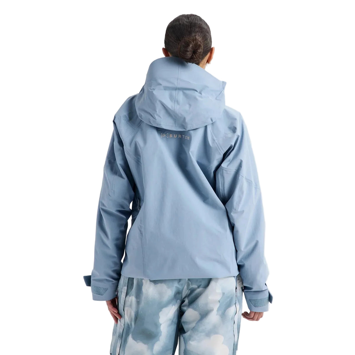 A person shown from the back wearing a light blue hooded jacket and matching blue patterned pants against a plain light gray studio background.