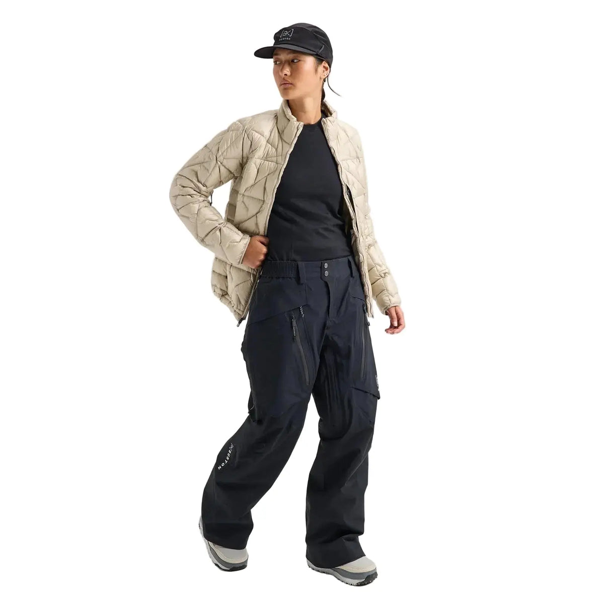A model wearing a beige quilted jacket, black t-shirt, black wide-leg cargo pants, and a black cap, standing against a light gray studio background.
